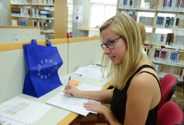 Eine junge Frau sitzt in einer Bibliothek und liest und schreibt dort.